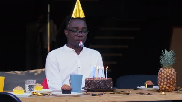 Zelfisolatie. Trieste eenzame Afrikaanse jonge knappe man blaast fluitje alleen vieren zijn eigen verjaardag met taart thuis — Stockvideo