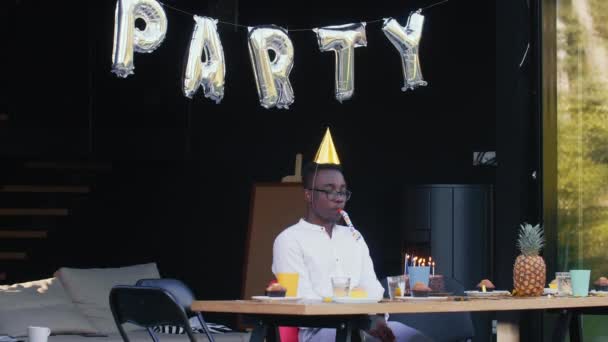 La vida social en cuarentena. Triste joven africano solitario celebrando su propio cumpleaños con pastel y velas en casa. — Vídeo de stock