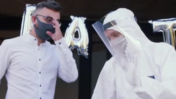 Close-up twee leuke gekke mannelijke vrienden dansen op COVID-19 stijl feest in witte medische veiligheid beschermende maskers en pakken. — Stockvideo