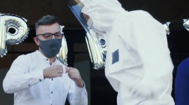 Yakın plan üç beyaz erkek arkadaş COVID-19 stil partisinde tıbbi güvenlik maskeleri ve kıyafetleriyle dans ediyor..