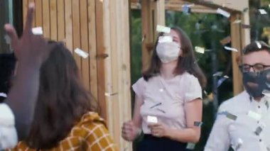 Arkadaşlar COVID-19 'dan sonra normal hayatı kutluyorlar. Eğlenceli konfeti partilerinde maskeli mutlu çoklu etnik gençler dans ediyor..