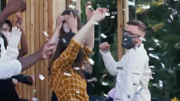 Vänner som firar återgång till det normala livet efter COVID-19 dansar på en rolig multietnisk fest under konfetti i ansiktsmasker. — Stockvideo