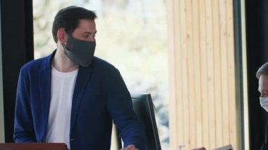 Pozitif genç iş adamları, COVID-19 sırasında koruyucu maske takarak moda ofis masasında birlikte çalışıyorlar..