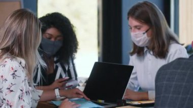 İş yerindeki COVID-19 salgın koruması olan kadınlar. Yüz maskeleriyle çalışan üç mutlu, etnik çeşitlilikte genç bayan meslektaşım var.