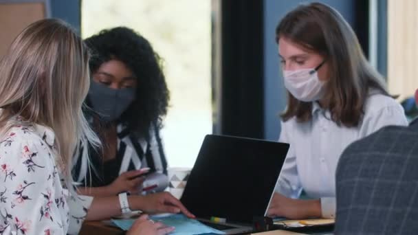 Mujeres en el lugar de trabajo con protección contra la epidemia de COVID-19. Tres jóvenes colegas jóvenes multiétnicos felices trabajan en máscaras faciales — Vídeos de Stock