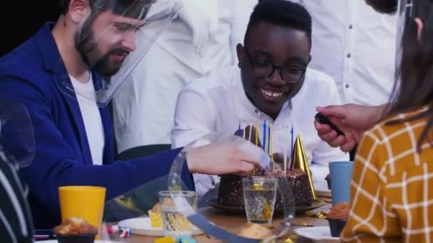 Glückliche junge multiethnische Freunde bereiten Geburtstagsfeier vor, zünden Kerzen auf Kuchen in COVID-19 Gesichtsschildern an. — Stockvideo