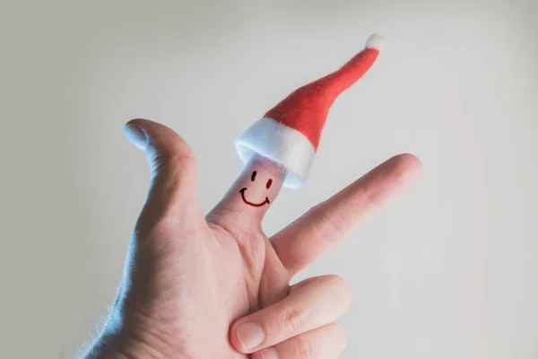 male hand with santa hat and smiley face on index finger