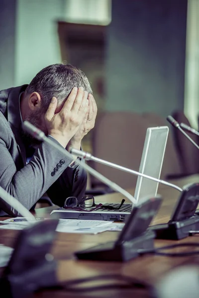 Sad businessman with beard working in office and covering his face