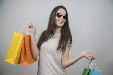 Alışveriş çantaları tutan güneş gözlüğü takan heyecanlı güzel bir kız portresi 