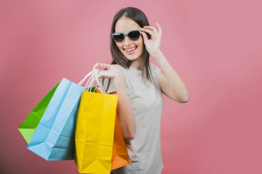 Alışveriş çantaları tutan güneş gözlüğü takan heyecanlı güzel bir kız portresi 