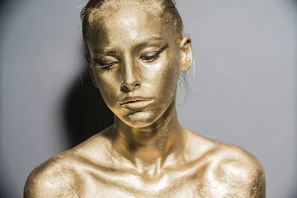 Fashion model woman golden skin face in bright sparkles, Trendy glowing gold skin make-up. Glitter metallic shine makeup
