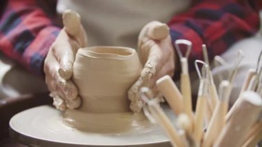 Potter 'ın elinin yakın çekimi Potter' ın tekerleğinde bir sürahi kil yontuyor.