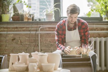Kendi atölyesinde yeni kil öğe üzerinde çalışan iş giyim genç başarılı çömlekçi
