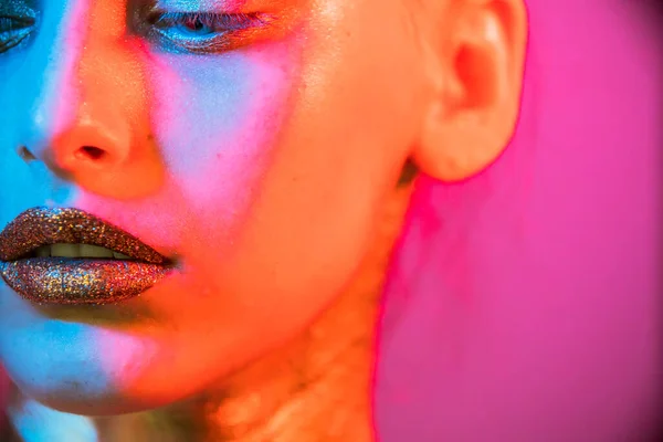 Fashion model metallic silver lips and face woman in neon uv blue and purple lights, posing in studio, beautiful girl, glowing make-up, colorful make up.