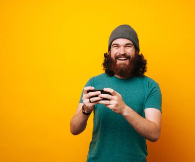 Neşeli gülümseyerek telefonu kullanarak ve kameraya bakarak hipster adam sakallı