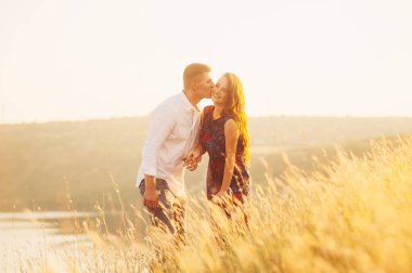 Genç çift çayır günbatımında zevk. Öpüşme ve gülümseyen aşk kaç içinde