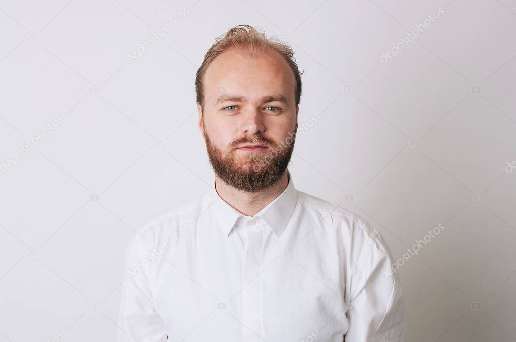Simple portrait of a young bearded man wearing a white shirt looking at the camera.