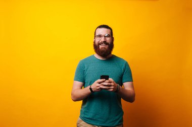 Onun telefon tutarak ve sarı arka plan kameraya gülümseyen gözlük, sakallı genç adam.