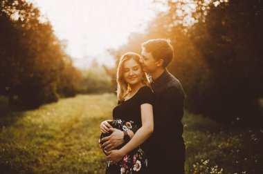 Mutlu hamile INLOVE çift gülümseyen ve oudoors sarılma.