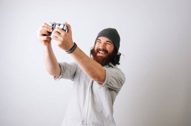 Genç bir selfie bir eski fotoğraf makinesi ile alarak hipster adam sakallı. Beyaz arka plan üzerinde mutlu gülümseyen adam. Fotoğrafçı hobi kavramı.
