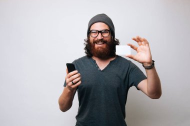 Neşeli gülümseyen smartphone ve kredi kartı holding, alışveriş online kavramı hipster adam sakallı