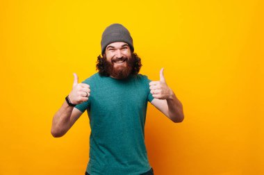 Mutlu gülen sarı arka plan üzerinde başparmak gösterilmesini hipster adam sakallı