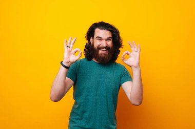 Mutlu genç hipster ok jest sarı arka plan üzerinde gösterilen kameraya gülümseyen.