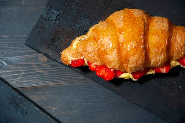 在黑色背景下的法式羊角面包与香草奶油和草莓切片的顶级视图 — 图库照片