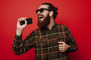 Şarkı ve müzik ile hücre telefon ve radyo earphones kırmızı duvardan izole mutlu sakallı hippi adam portresi