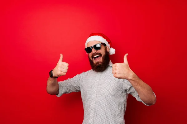 冬の休日とカウント ダウンの概念 ひげを持つ男と陽気な顔は クリスマスを祝います サンタ クロースは 赤の背景に新年を待ちます サンタ 表示中の親指 — ストック写真