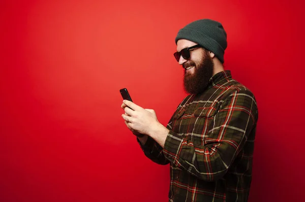 Glada Unga Skäggiga Hipster Mannen Med Smartphone Röd Bakgrund — Stockfoto