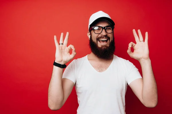 Fröhlicher Mann Mit Bart Zeigt Geste Vor Rotem Hintergrund — Stockfoto