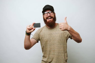 Gözlük takan ve başparmak gösterilmesini ve kredi kartı tutan sakallı neşeli adam