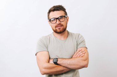 Beyaz arka plan üzerinde kameraya bakarak çapraz kollu yakışıklı genç sakallı adam portresi