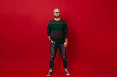 Kırmızı arka plan üzerinde duran ve kameraya bakarak sakallı hippi adam portresi tam uzunlukta