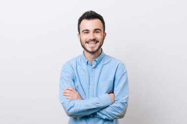 Casual beyaz arka plan üzerinde gülümseyen ve kameraya bakarak çapraz kolları olan neşeli genç adam portresi