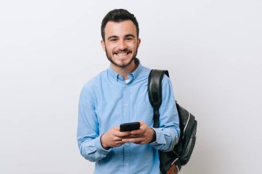 Casual smartphone holding ve kamera ayakta beyaz duvardan arıyor genç adam gülümseyen portresi