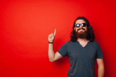 Sakal ve kırmızı arka plan üzerinde yukarıyı güneş gözlüğü ile neşeli adam