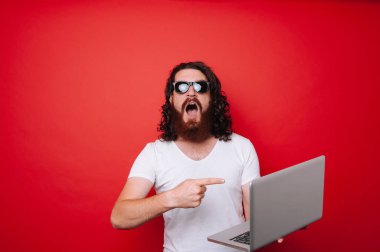 Laptop kırmızı arka plan üzerinde işaret heyecanlı sakallı adam