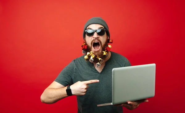 Amazed bearded man pointing at laptop over red background