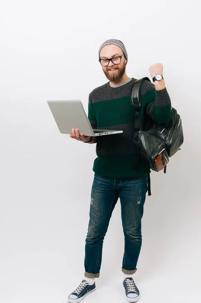 Full lenght portrait of bearded hipster man using laptop and celebrating success over white background