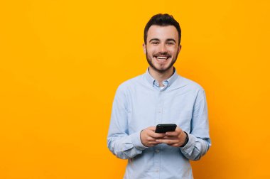 Neşeli genç adam rahat kullanarak telefon sarı arka plan üzerinde
