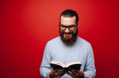 Kırmızı arka plan üzerinde bir kitap okuma rahat sakallı neşeli adam portresi