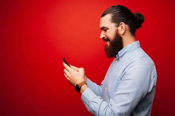 Happy man with beard texting in a mobile phone over red background