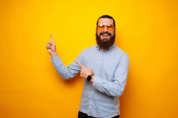 Smiling and happy bearded man pointing away at copyspace over yellow background