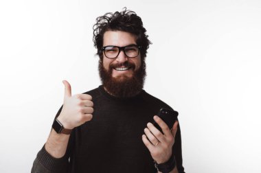 Başparmak gösterilmesini ve telefon tutarak yakışıklı gülümseyen sakallı adam