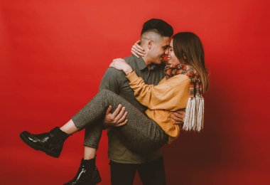 Mutlu genç INLOVE çift kırmızı bir arka plan üzerinde. Eşi, gülümseyen kız arkadaşı kollarında tutan adam. Sevgi, Aile ve Sevgililer günü kavramı.