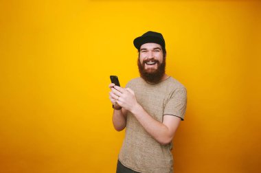 Güzel telefon sarı arka plan üzerinde tipik haber ve gülümseyen hipster adam sakallı