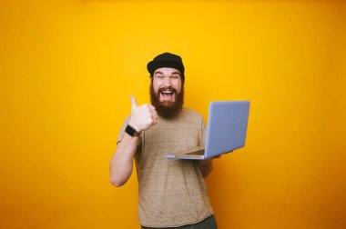Dizüstü tutarak ve başparmak sarı arka plan üzerinde gösterilen sakallı gülümseyen adam portresi