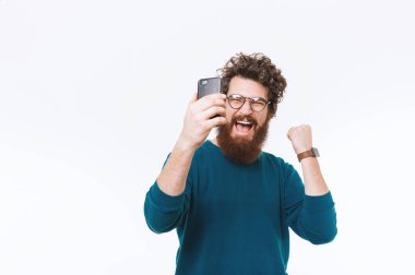 Smartphone vasıl arıyorsunuz ve başarı beyaz arka plan üzerinde kutluyor hayret ve neşeli sakallı adam